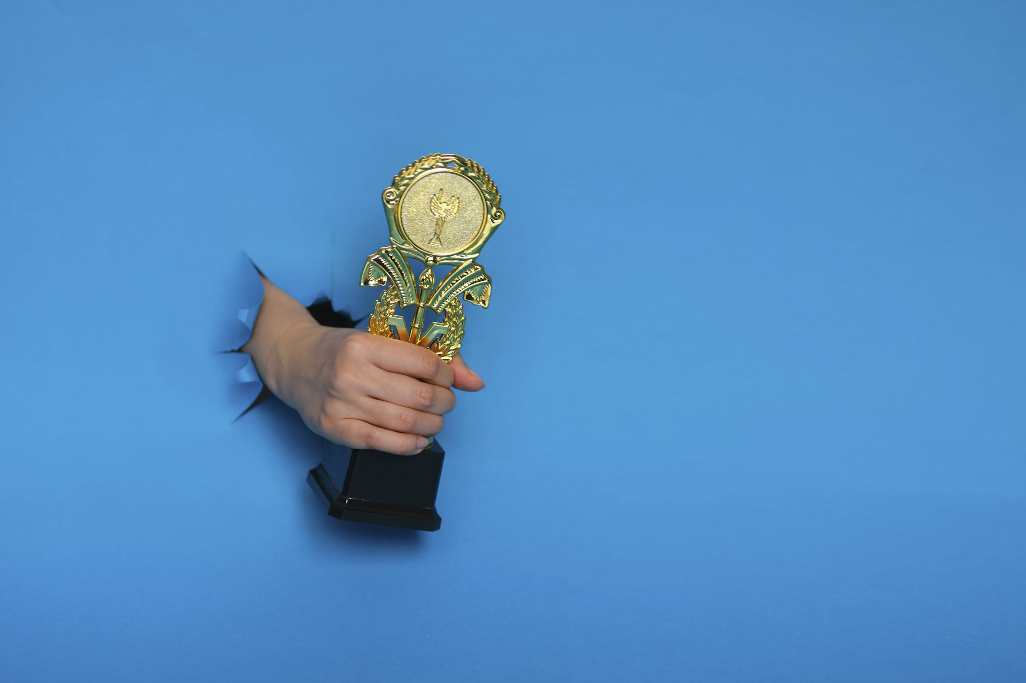 image of trophy in hand, concept for winning or success. Golden trophy on blue background, top view